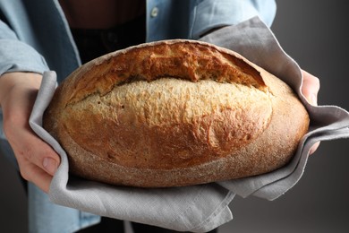 Photo of Woman with loaf of freshly baked bread on grey background, closeup