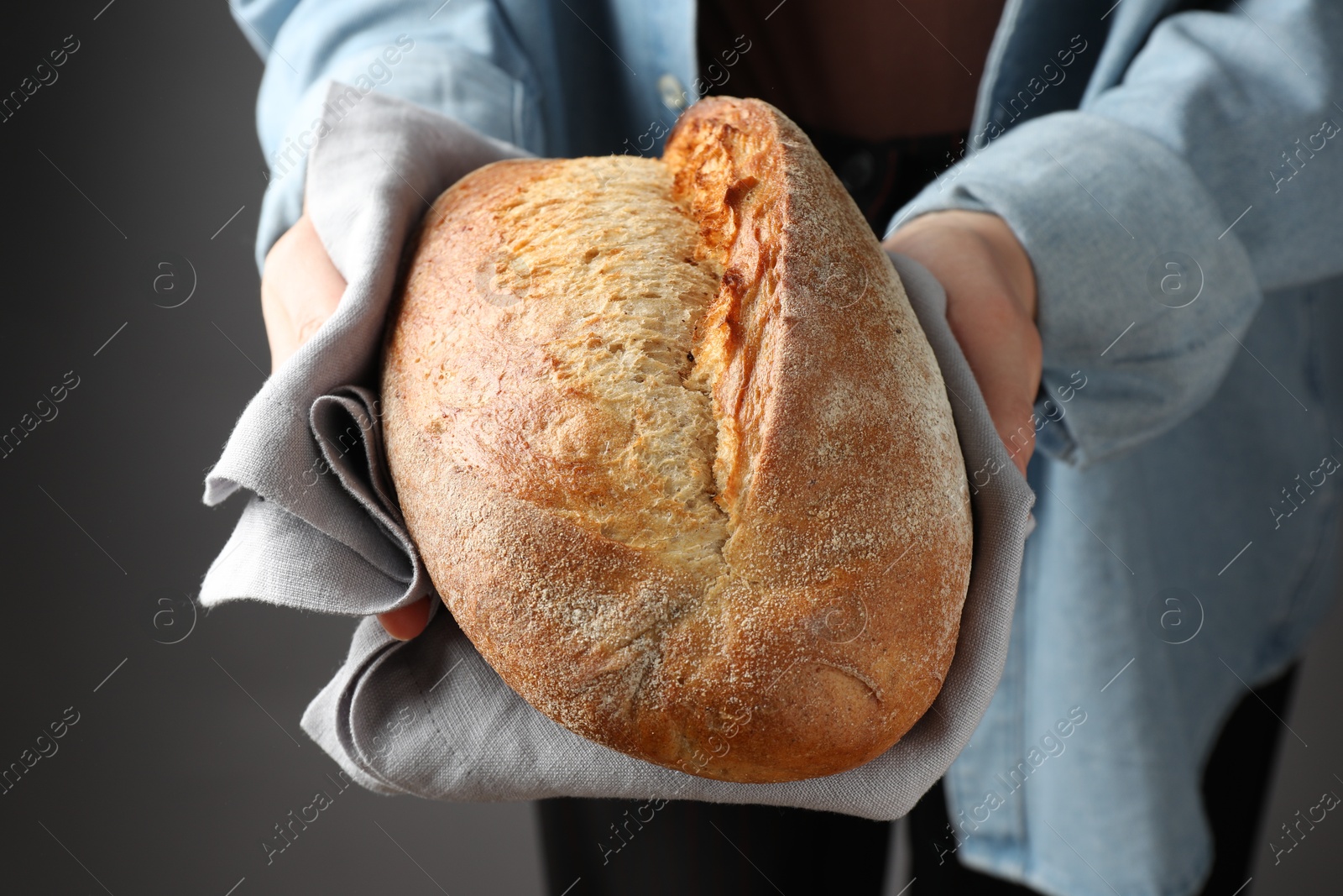 Photo of Woman with loaf of freshly baked bread on grey background, closeup