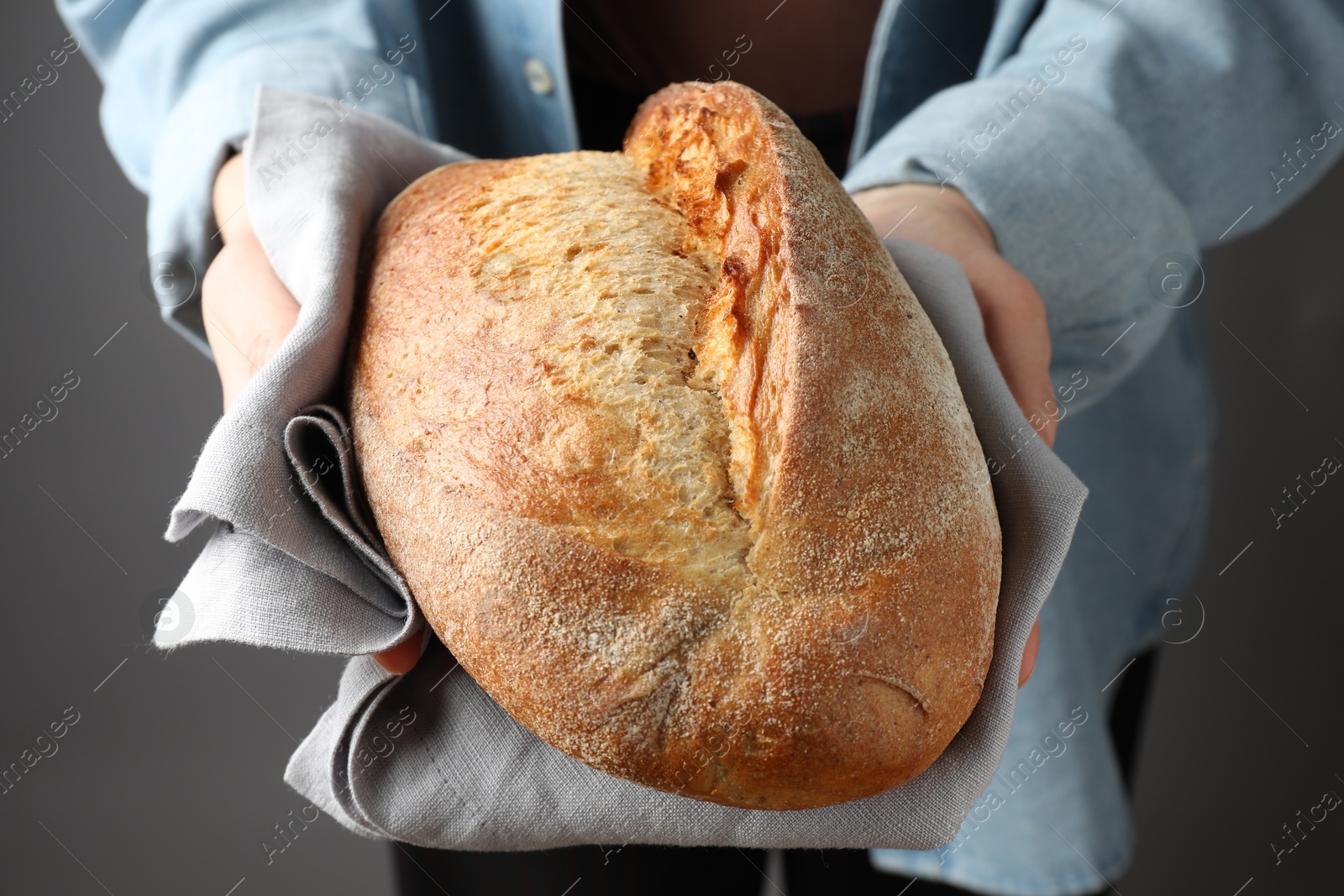 Photo of Woman with loaf of freshly baked bread on grey background, closeup