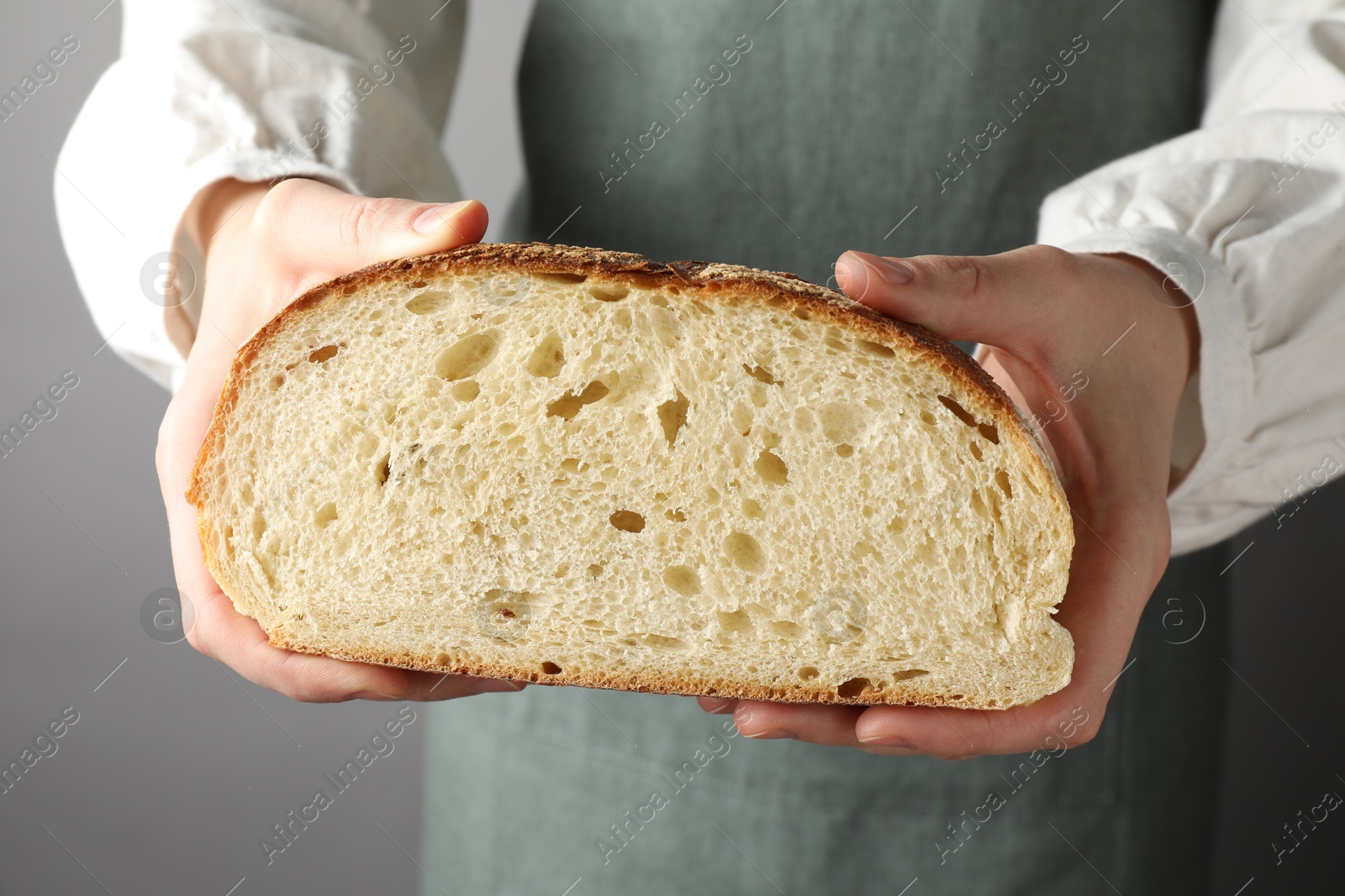 Photo of Woman with piece of fresh bread on grey background, closeup