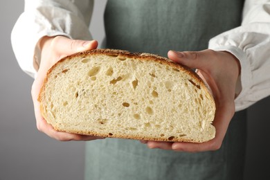 Photo of Woman with piece of fresh bread on grey background, closeup