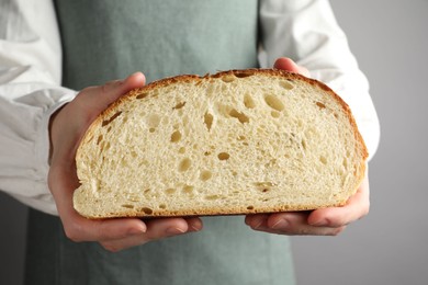 Photo of Woman with piece of fresh bread on grey background, closeup