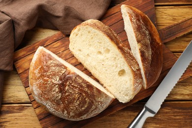 Photo of Cut loaf of fresh bread and knife on wooden table, top view