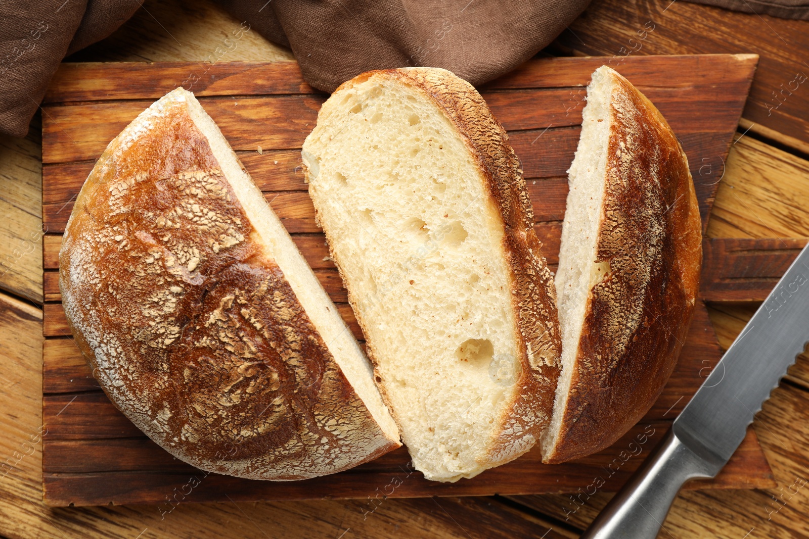 Photo of Cut loaf of fresh bread and knife on wooden table, top view