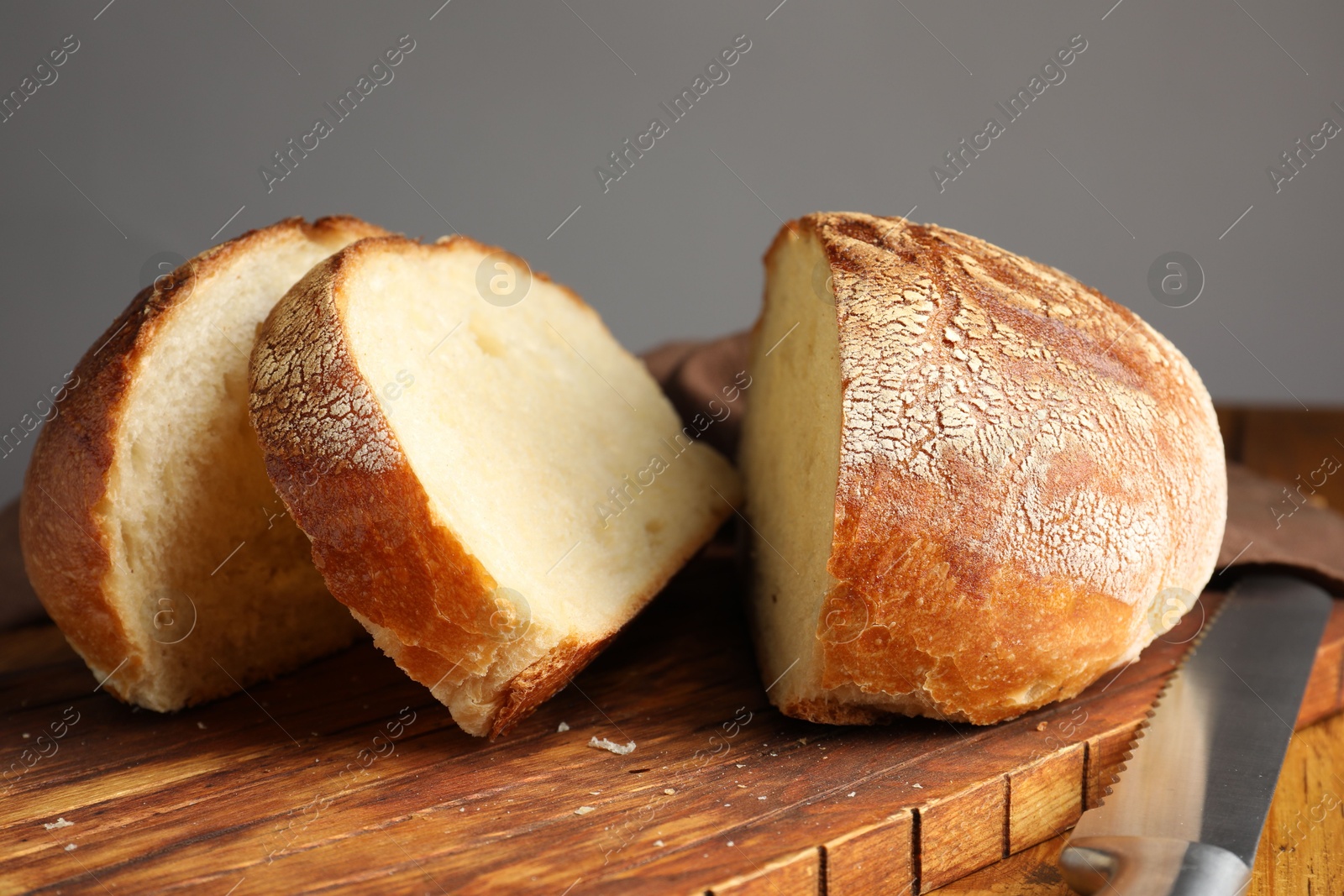 Photo of Cut loaf of fresh bread and knife on wooden table, closeup