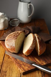 Photo of Cut loaf of fresh bread and knife on wooden table