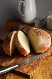 Photo of Cut loaf of fresh bread and knife on wooden table