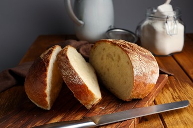 Photo of Cut loaf of fresh bread and knife on wooden table, closeup