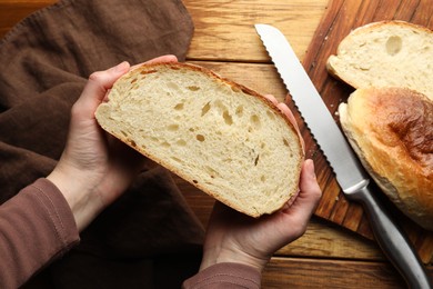 Photo of Woman with piece of fresh bread at wooden table, top view