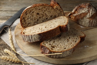 Photo of Cut loaf of fresh bread and knife on wooden table, closeup