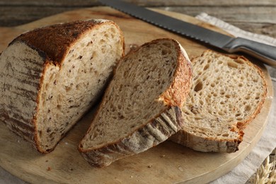 Photo of Cut loaf of fresh bread and knife on wooden table, closeup