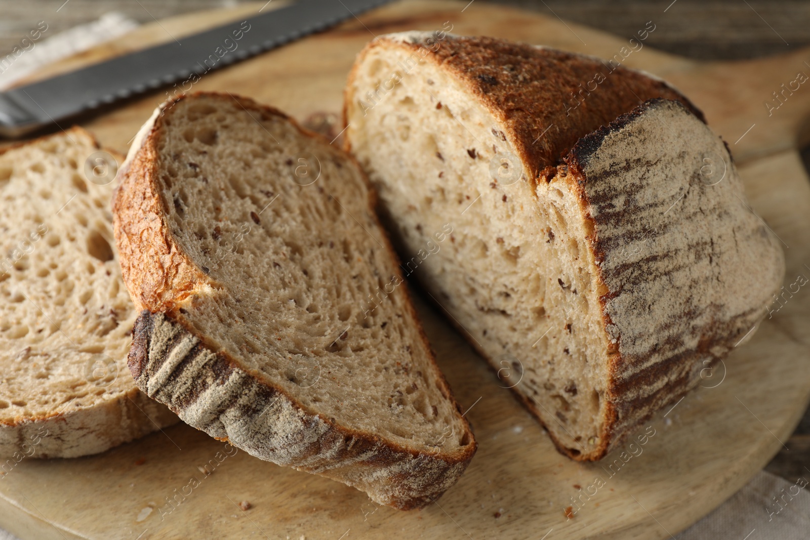 Photo of Cut loaf of fresh bread and knife on wooden table, closeup