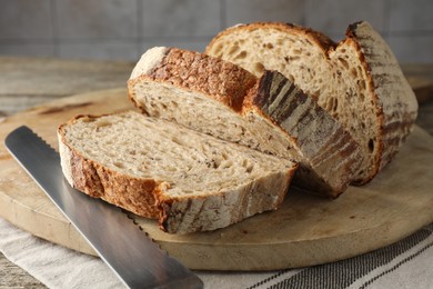 Photo of Cut loaf of fresh bread and knife on table, closeup