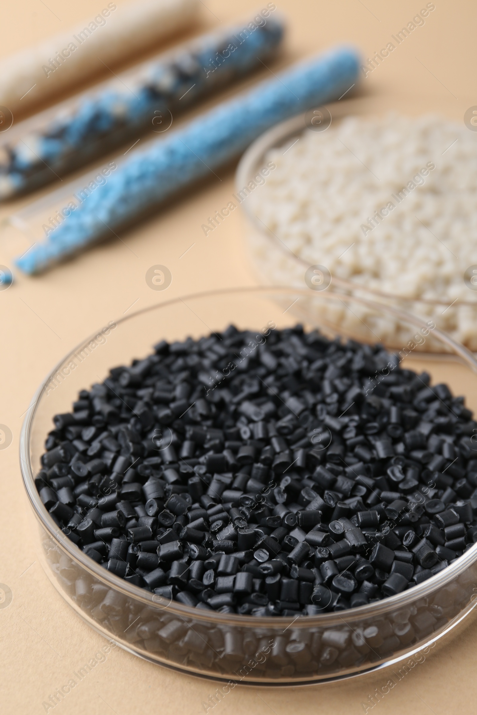 Photo of Colorful plastic granules in petri dishes and test tubes on beige background, closeup