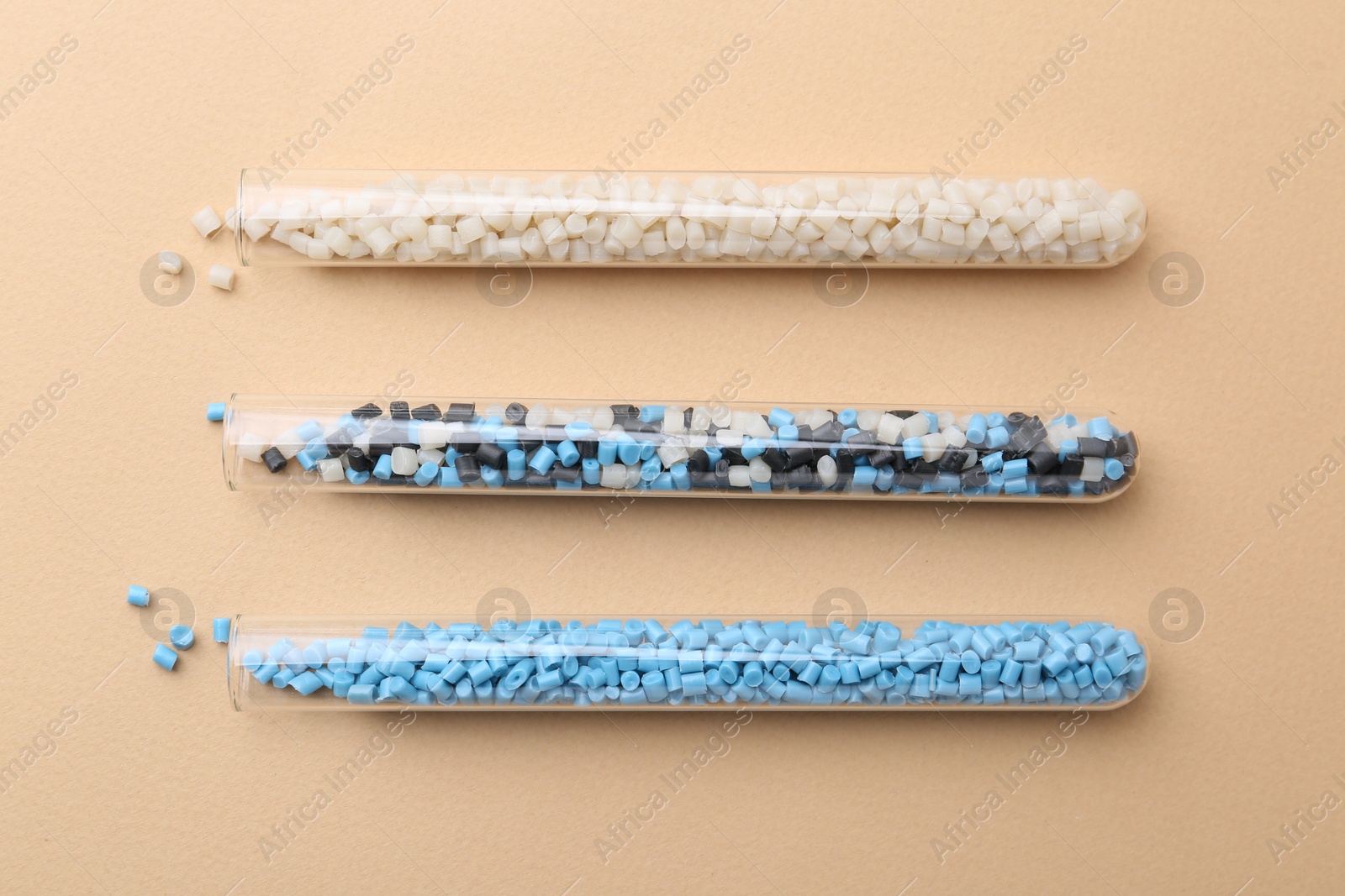 Photo of Colorful plastic granules in test tubes on beige background, flat lay