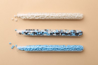 Colorful plastic granules in test tubes on beige background, flat lay