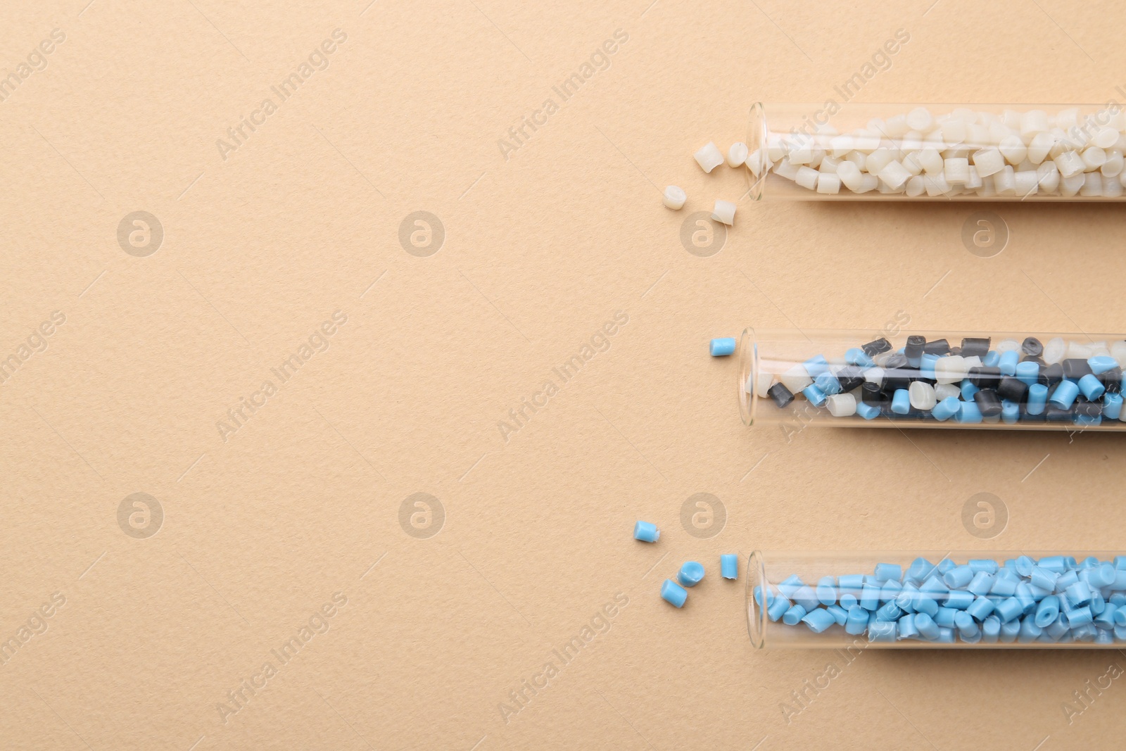 Photo of Colorful plastic granules in test tubes on beige background, flat lay. Space for text