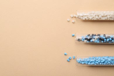 Photo of Colorful plastic granules in test tubes on beige background, flat lay. Space for text