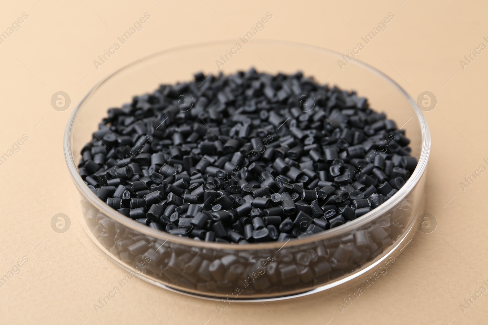 Photo of Black plastic granules in petri dish on beige background, closeup