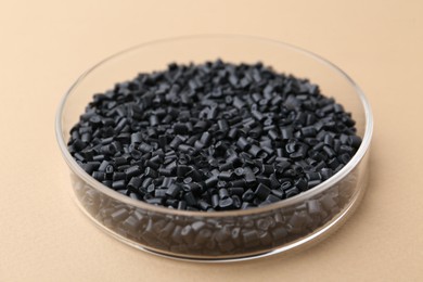 Photo of Black plastic granules in petri dish on beige background, closeup