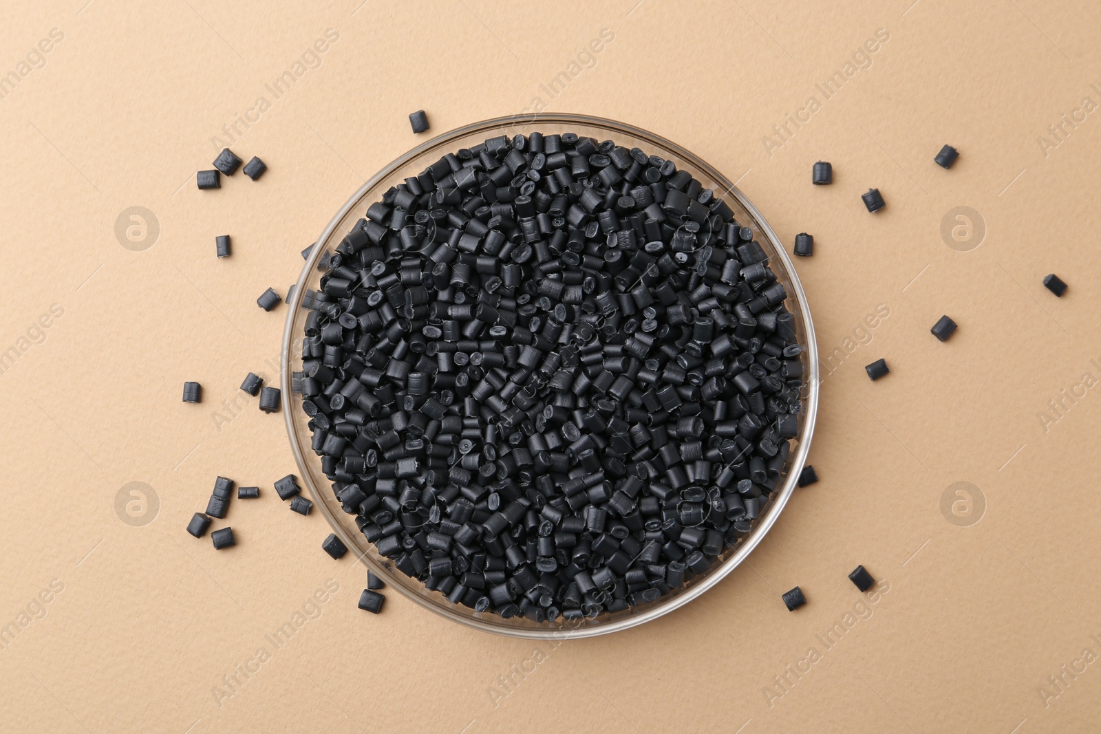 Photo of Black plastic granules in petri dish on beige background, top view