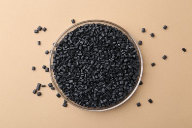 Photo of Black plastic granules in petri dish on beige background, top view