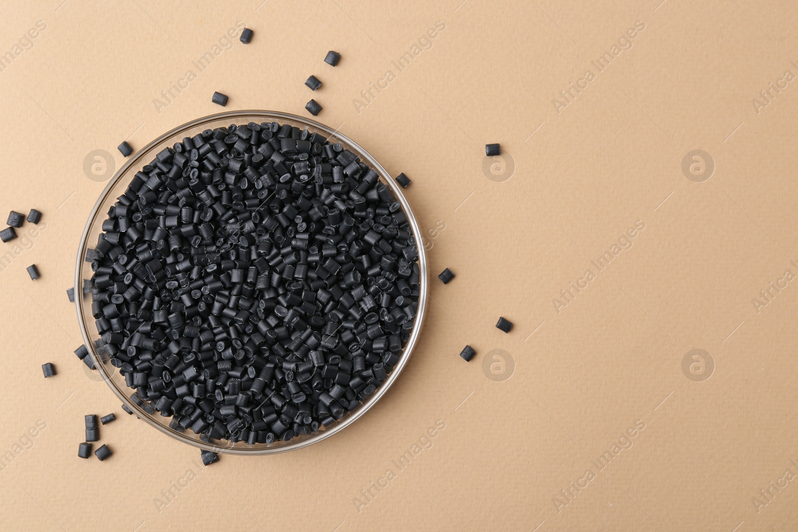 Photo of Black plastic granules in petri dish on beige background, top view. Space for text