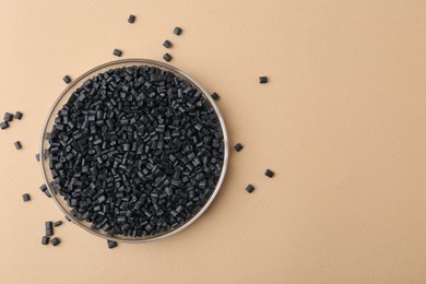 Photo of Black plastic granules in petri dish on beige background, top view. Space for text