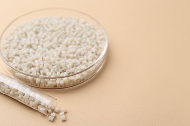 Plastic granules in petri dish and test tube on beige background, closeup. Space for text