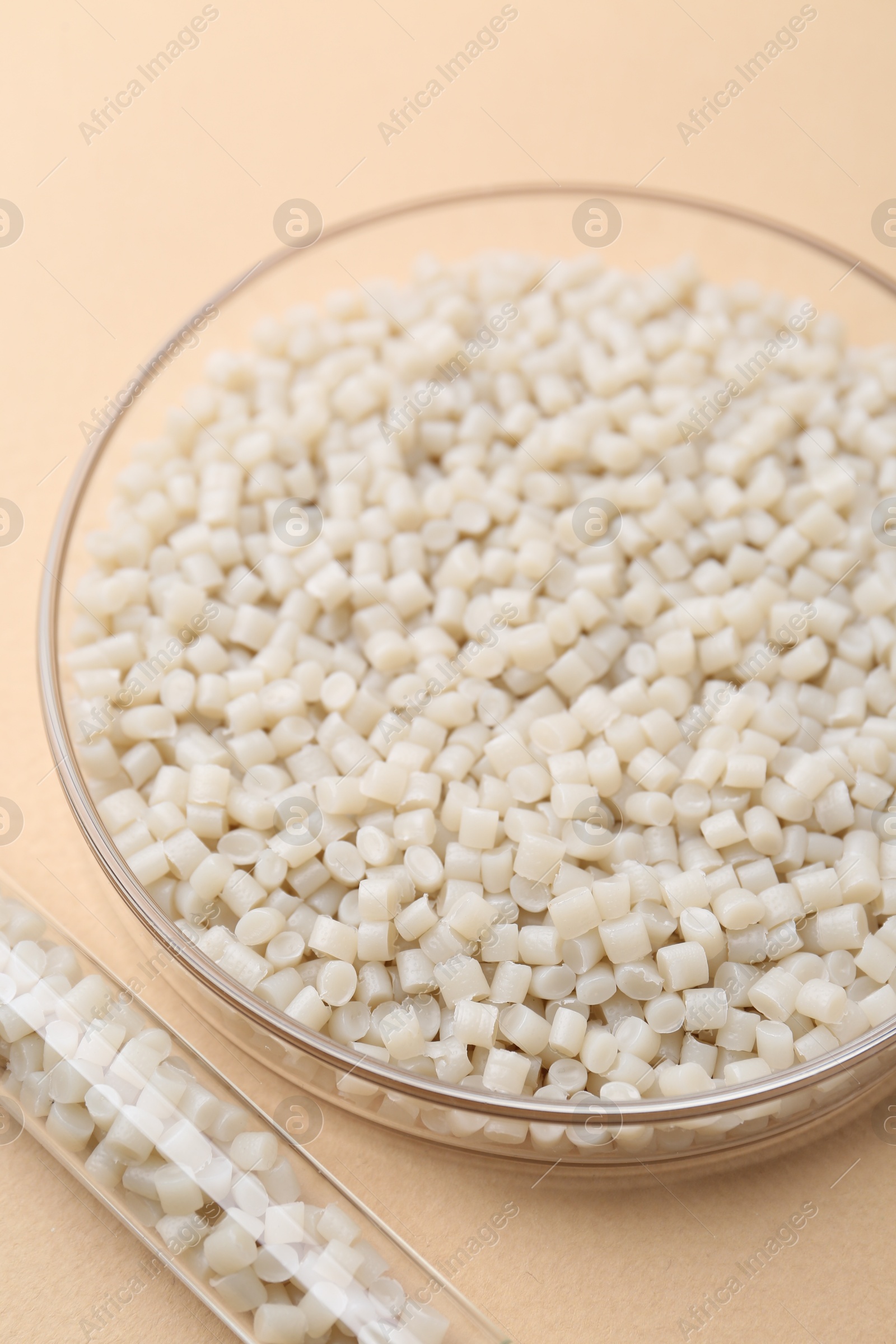 Photo of Plastic granules in petri dish and test tube on beige background, closeup