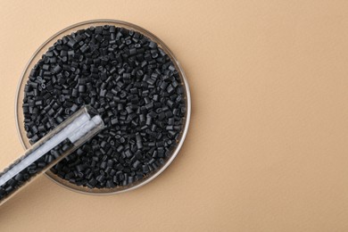 Black plastic granules in petri dish and test tube on beige background, top view. Space for text