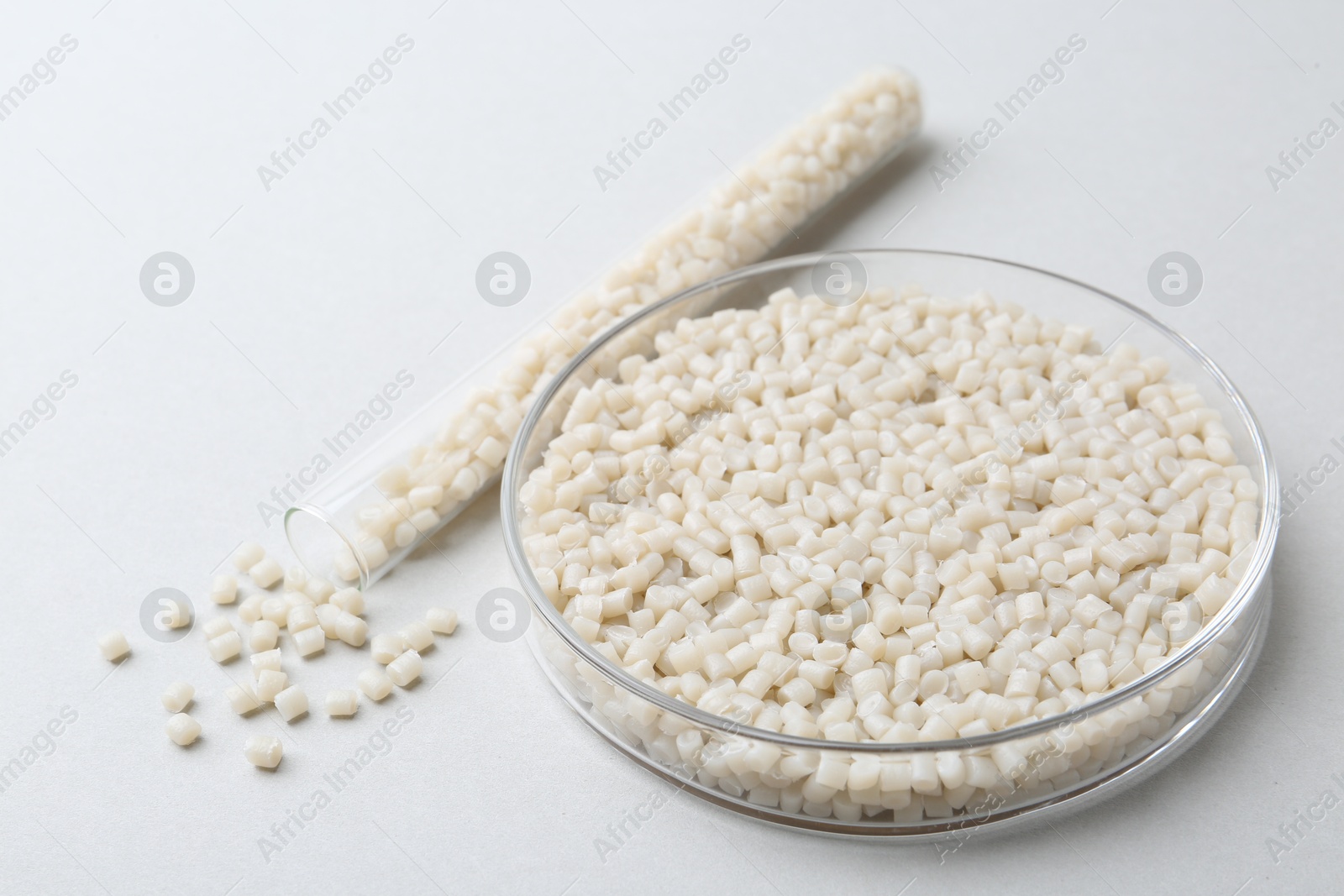 Photo of Plastic granules in petri dish and test tube on gray background, closeup