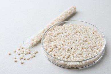 Plastic granules in petri dish and test tube on gray background, closeup