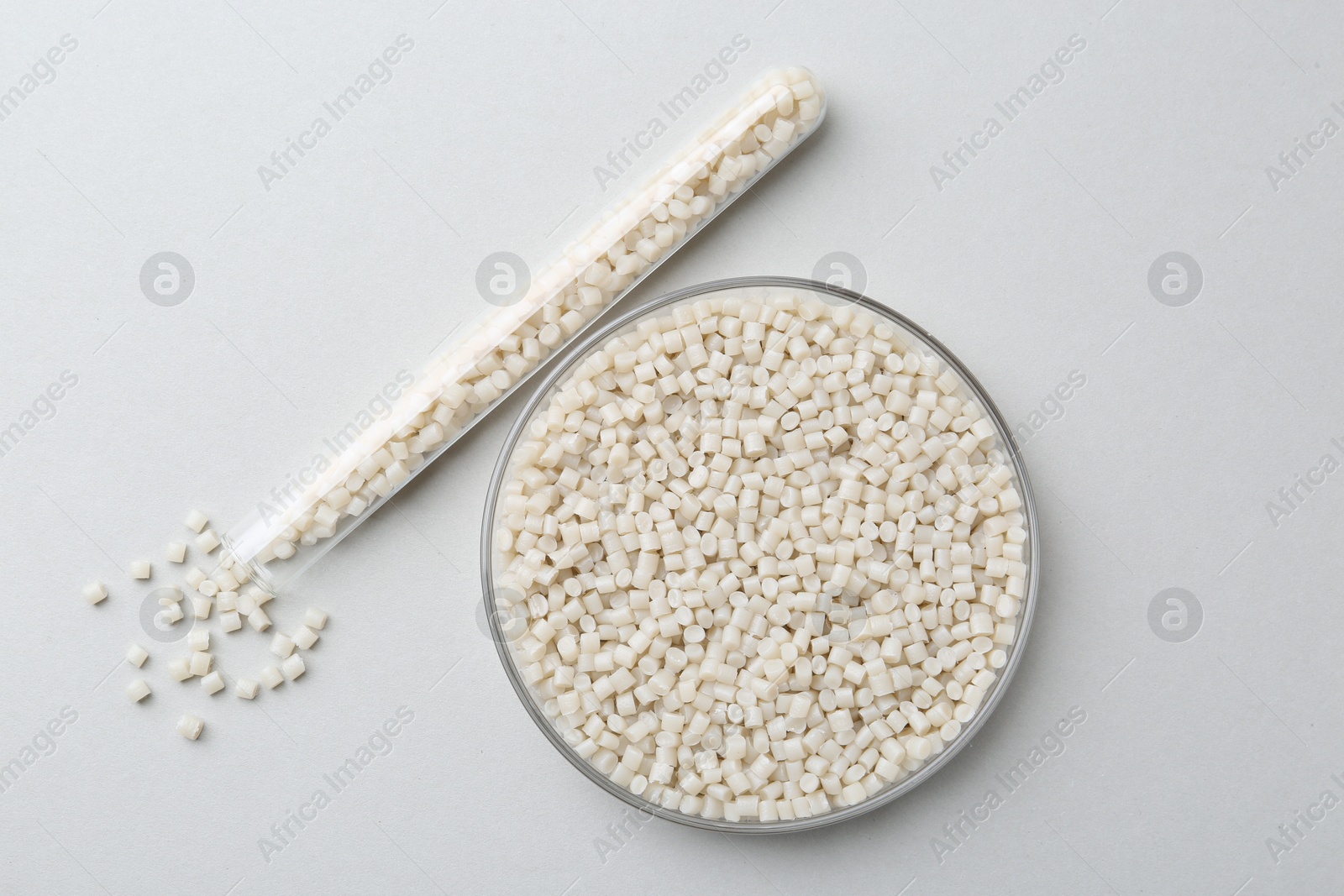 Photo of Plastic granules in petri dish and test tube on gray background, flat lay