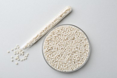 Photo of Plastic granules in petri dish and test tube on gray background, flat lay