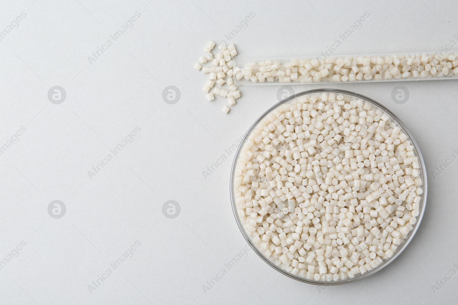 Photo of Plastic granules in petri dish and test tube on gray background, flat lay. Space for text