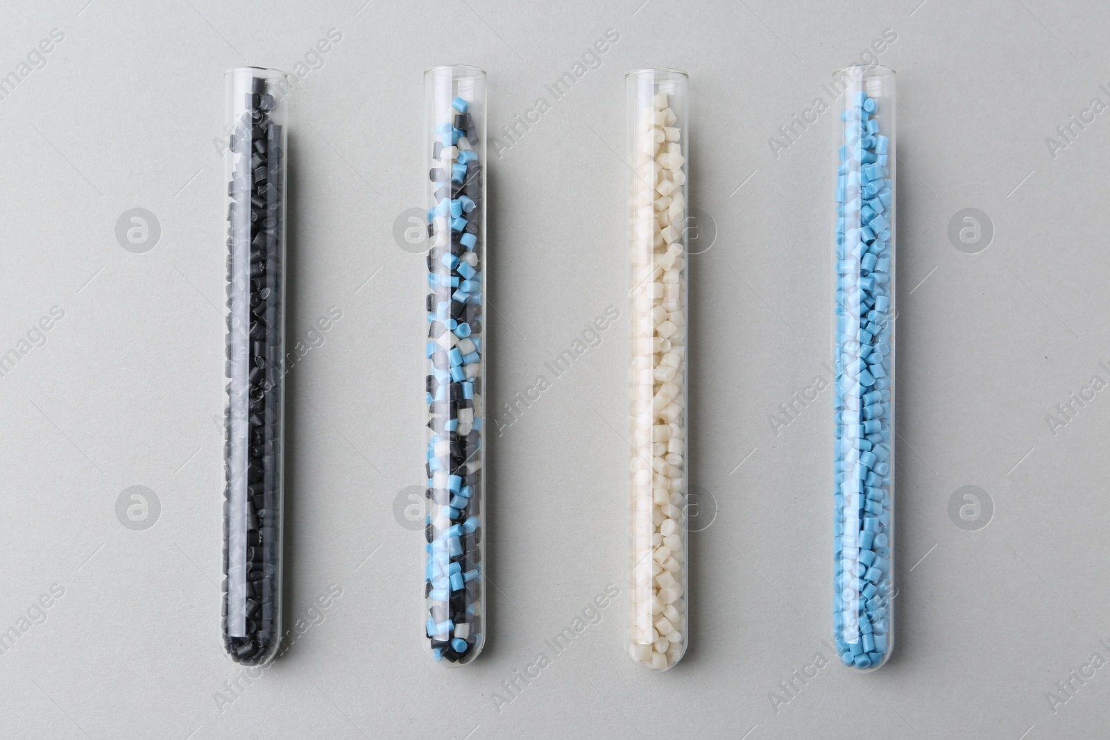 Photo of Colorful plastic granules in test tubes on gray background, flat lay