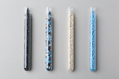 Colorful plastic granules in test tubes on gray background, flat lay