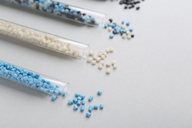 Colorful plastic granules in test tubes on gray background, closeup. Space for text