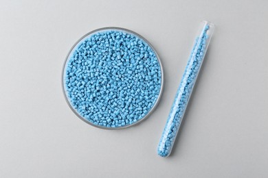 Light blue plastic granules in petri dish and test tube on gray background, flat lay