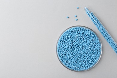 Light blue plastic granules in petri dish and test tube on gray background, flat lay. Space for text