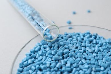 Light blue plastic granules in petri dish and test tube on gray background, closeup