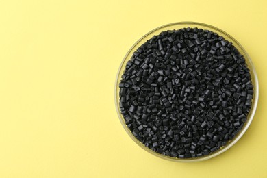 Black plastic granules in petri dish on yellow background, top view. Space for text