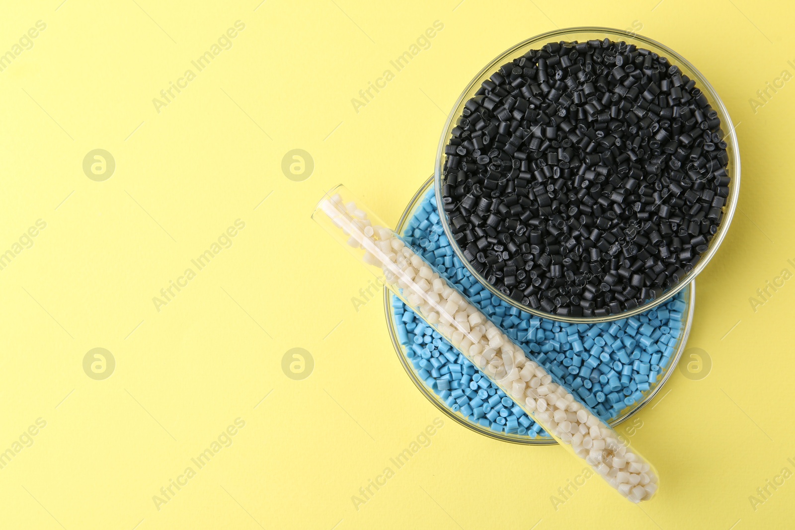 Photo of Colorful plastic granules in petri dishes and test tube on yellow background, top view. Space for text