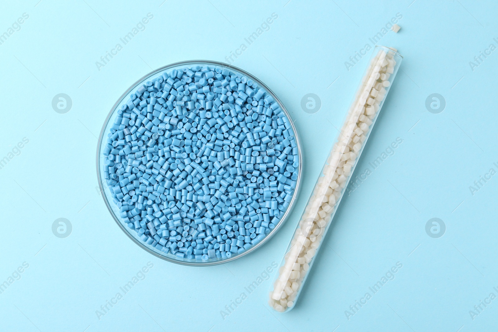 Photo of Colorful plastic granules in petri dish and test tube on light blue background, flat lay