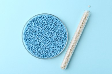 Colorful plastic granules in petri dish and test tube on light blue background, flat lay