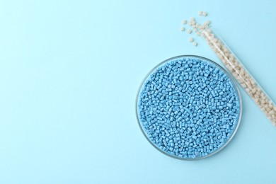 Photo of Colorful plastic granules in petri dish and test tube on light blue background, flat lay. Space for text