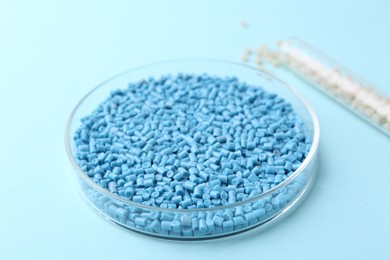 Colorful plastic granules in petri dish and test tube on light blue background, closeup