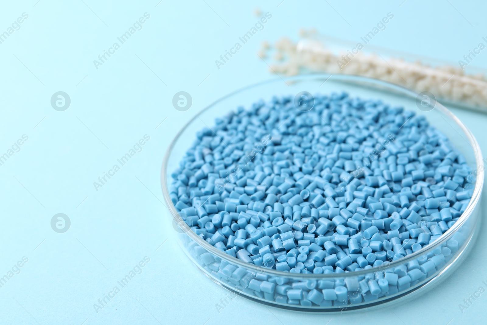 Photo of Colorful plastic granules in petri dish and test tube on light blue background, closeup. Space for text