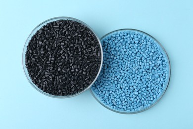 Colorful plastic granules in petri dishes on light blue background, top view